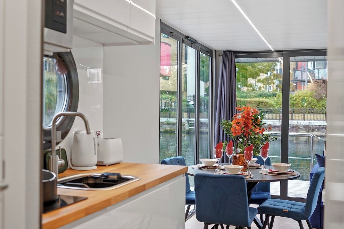 A modern kitchen with a dining area, large windows, and a view of a body of water.