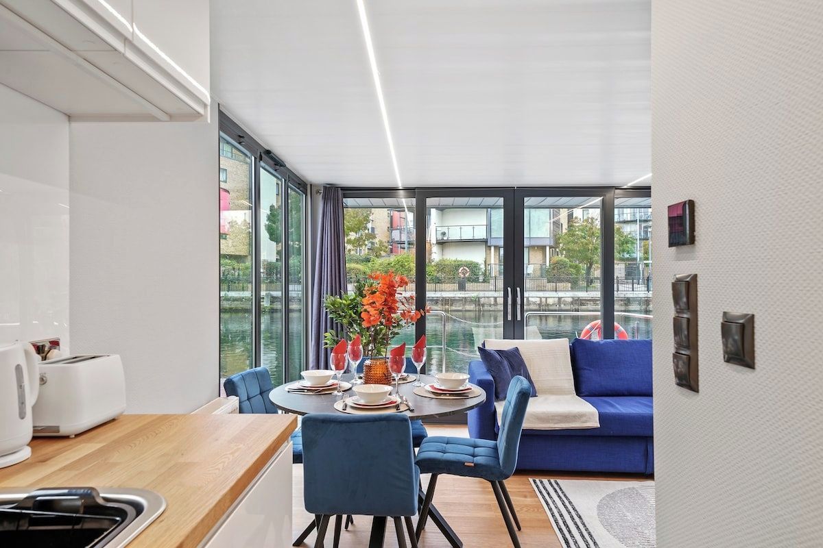 A modern kitchen with a dining area, a blue sofa, and a view of the city through large windows.