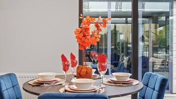 A dining table set for four with a vase of orange flowers, red napkins, and white plates.