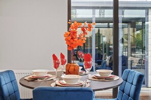 A dining table set for four with a vase of orange flowers, red napkins, and white plates.