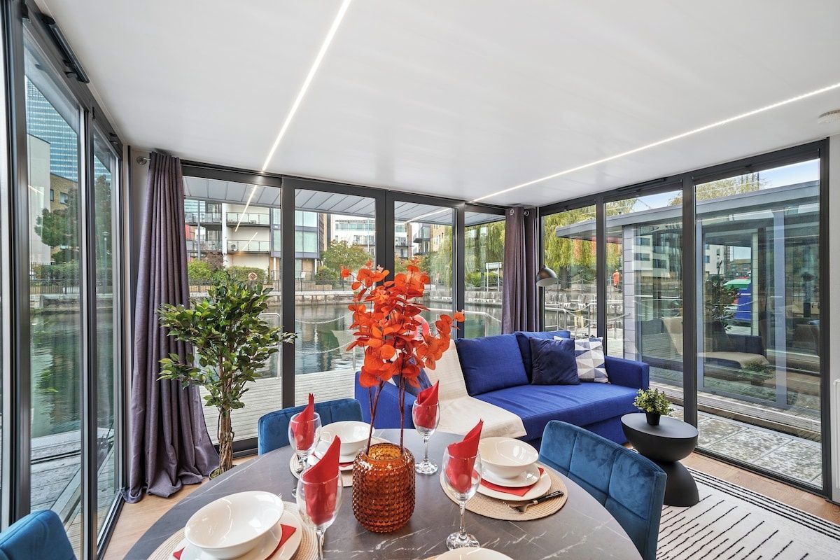 A modern dining area with a round table, blue seating, and large windows offering a view of the city.