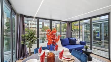 A modern dining area with a round table, blue seating, and large windows offering a view of the city.