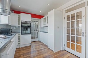 A modern kitchen with white cabinetry, a built-in oven, and a wooden floor. - Stylish Suburban Escape - Perivale Haven (London)