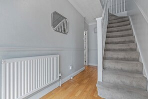 Eine Treppe mit Teppichstufen führt zu einer Zwischenebene, dort befindet sich ein weißer Heizkörper und ein Wandspiegel.