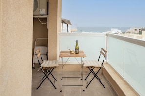 Ein Balkon mit zwei Stühlen, einem Tisch, einer Weinflasche und Blick auf das Meer.