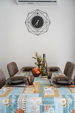 Ein Esstisch mit einer geometrischen Wanduhr, einer Blumenvase und einer Weinflasche.