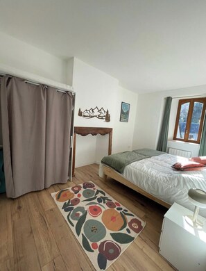 Ein Schlafzimmer mit einem Bett, einem kleinen Tisch, einem Fenster und einem Vorhang.