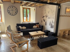 Ein gemütliches Wohnzimmer mit einer Couch, einem Holztisch, einem schwarzen Hocker, einem Holzschaukelstuhl und einer großen Wanduhr.