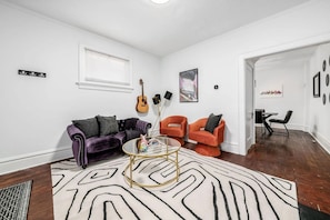 A living room with a purple sofa, orange chairs, a glass coffee table, and a patterned rug.