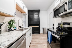 A modern kitchen with white cabinetry, a black door, stainless steel appliances, and a marble countertop.
