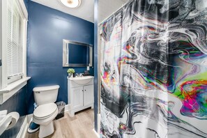 Ein Badezimmer mit blauer Wand, weißen Sanitärobjekten und einem großen abstrakten Wandbild.