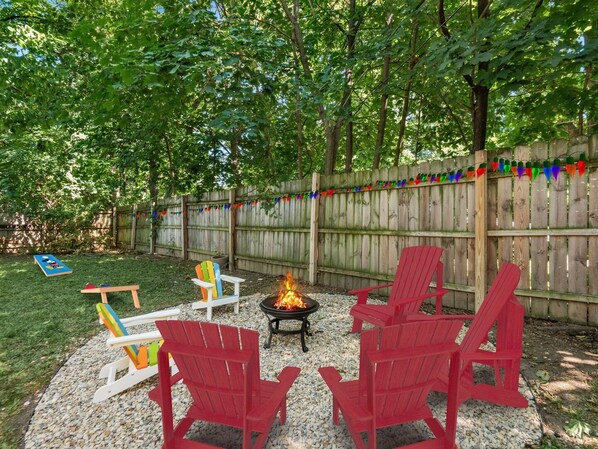 A backyard with a fire pit, red Adirondack chairs, a wooden playset, and a wooden fence.