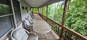 A covered porch with a view of a forest. There are white chairs and a table. - Secluded 2 BR Mountain Creeksong Cottage with Beautiful Fall Color Views (Burnsville)