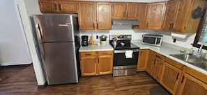 A kitchen with wooden cabinets, a stainless steel refrigerator, a microwave, and a stove. - Secluded 2 BR Mountain Creeksong Cottage with Beautiful Fall Color Views (Burnsville)