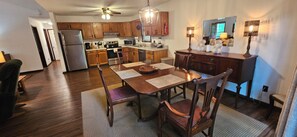 A modern kitchen with wooden cabinets, a dining table with chairs, and a refrigerator. - Secluded 2 BR Mountain Creeksong Cottage with Beautiful Fall Color Views (Burnsville)
