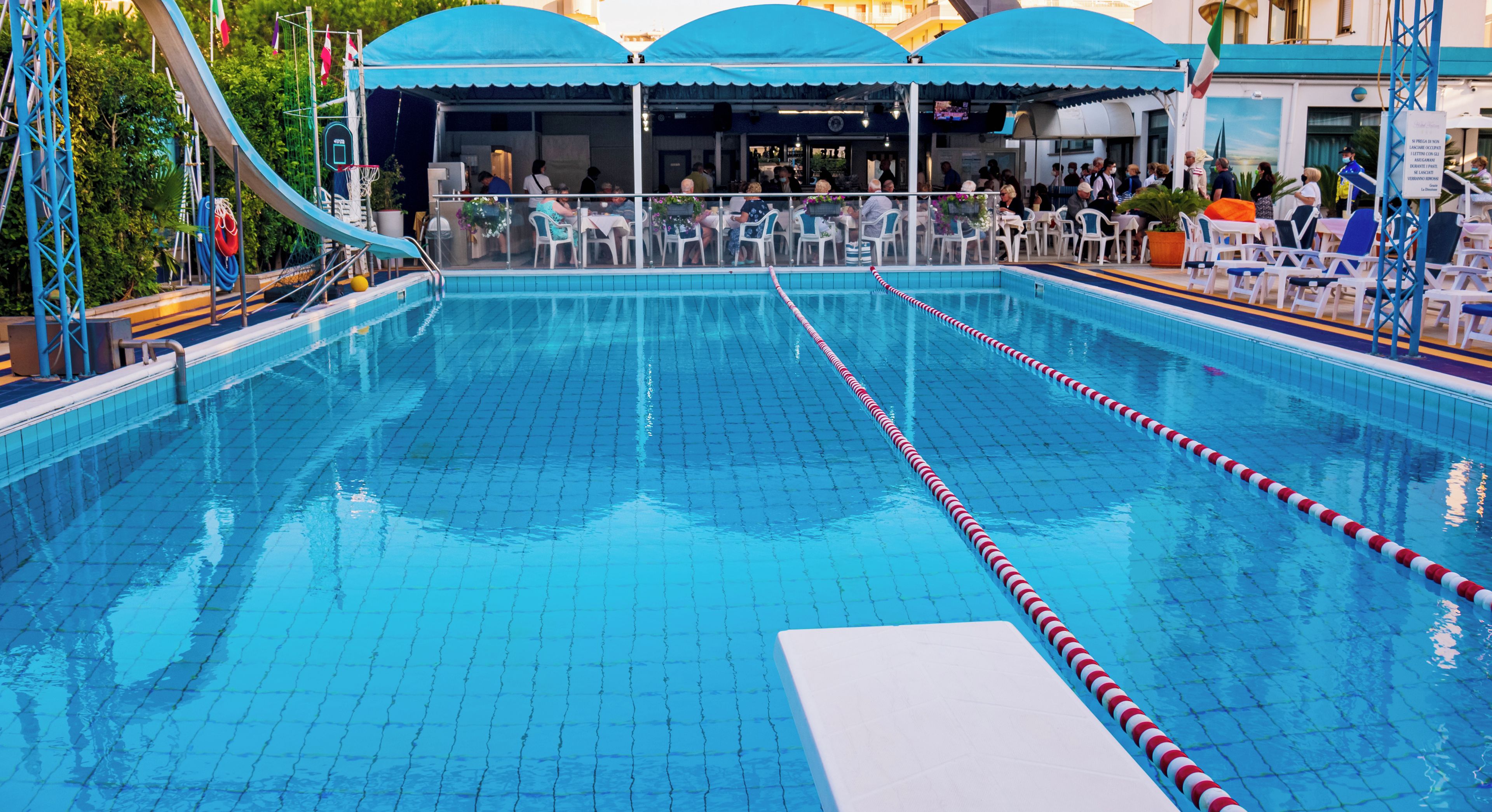 Una piscina con carriles delimitados, rodeada de asientos exteriores y una zona cubierta.