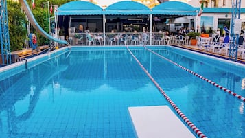 Una piscina con carriles delimitados, rodeada de asientos exteriores y una zona cubierta.