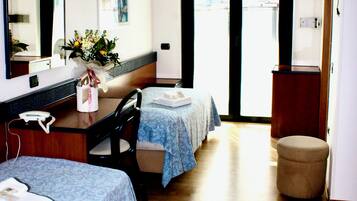 Habitación de hotel con dos camas, un escritorio, una silla, un pequeño reposapiés, un espejo y una puerta que da al exterior.