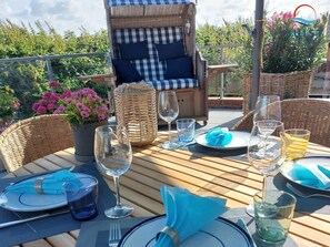 Ein Essbereich im Freien mit Korbmöbeln, einem Tisch für zwei Personen und Blick auf den Garten.