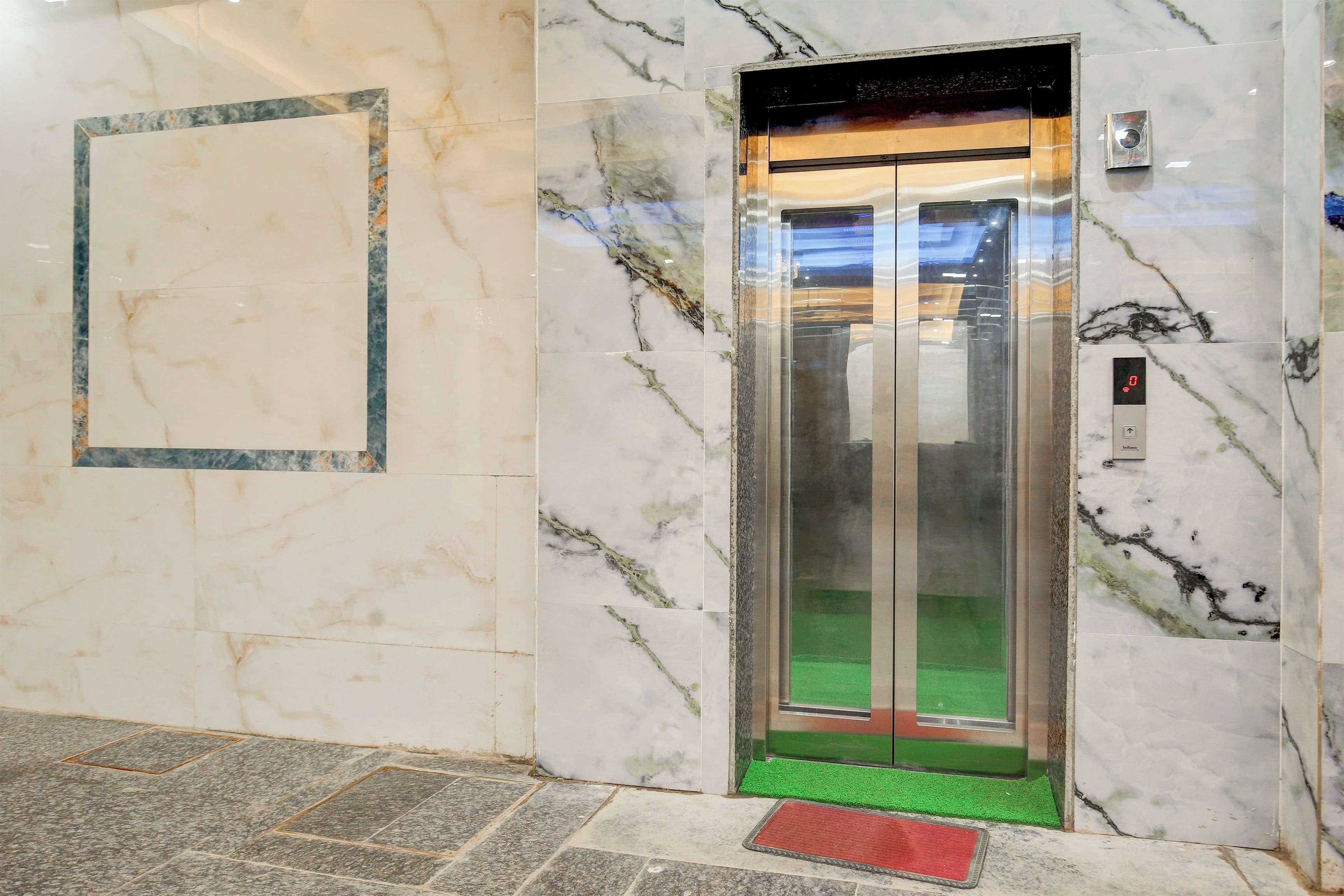 Un ascensor con un tapete verde en el suelo y un tapete rojo en la entrada, rodeado de paredes de mármol.