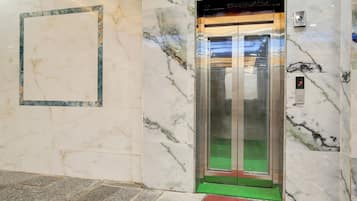 Un ascensor con un tapete verde en el suelo y un tapete rojo en la entrada, rodeado de paredes de mármol.