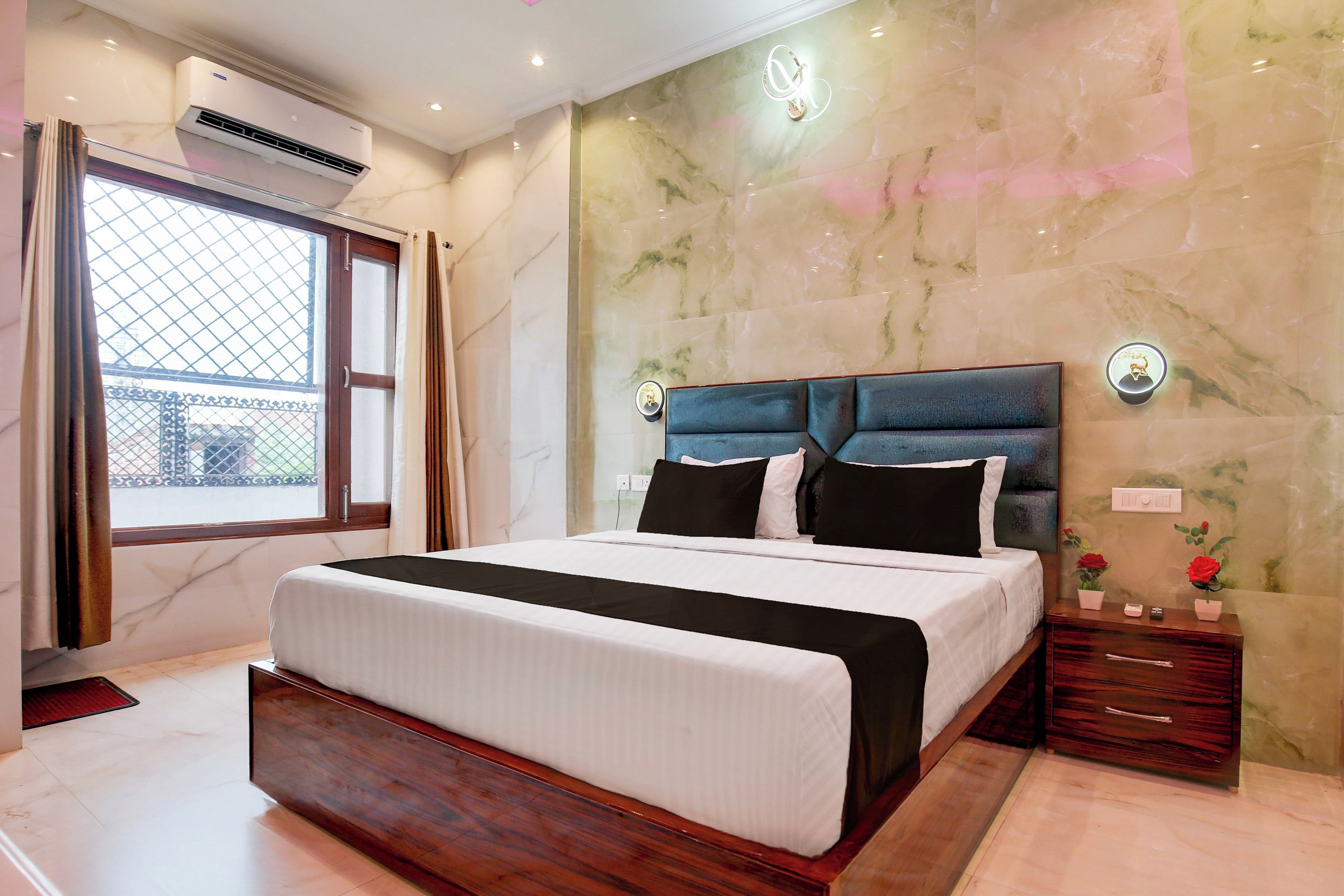 Quarto de hotel com cama grande, parede de mármore, ar condicionado e janela com cortinas.