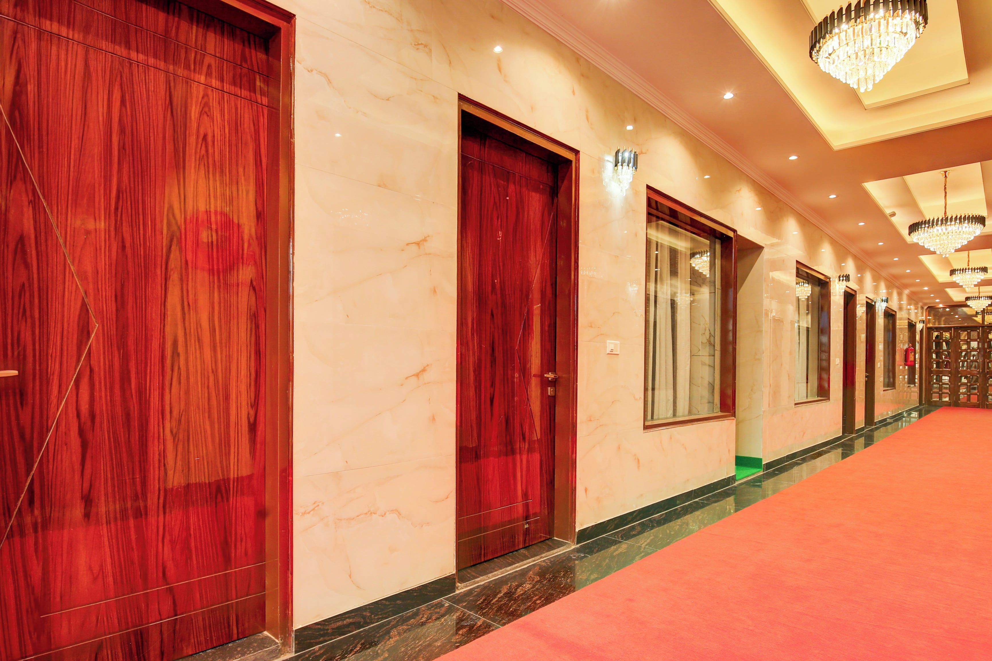 Corredor de hotel com paredes de mármore, portas de madeira e tapete vermelho.