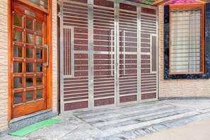Entrada de un edificio con puerta de recepción, un gran portón metálico y una ventana con cortina.
