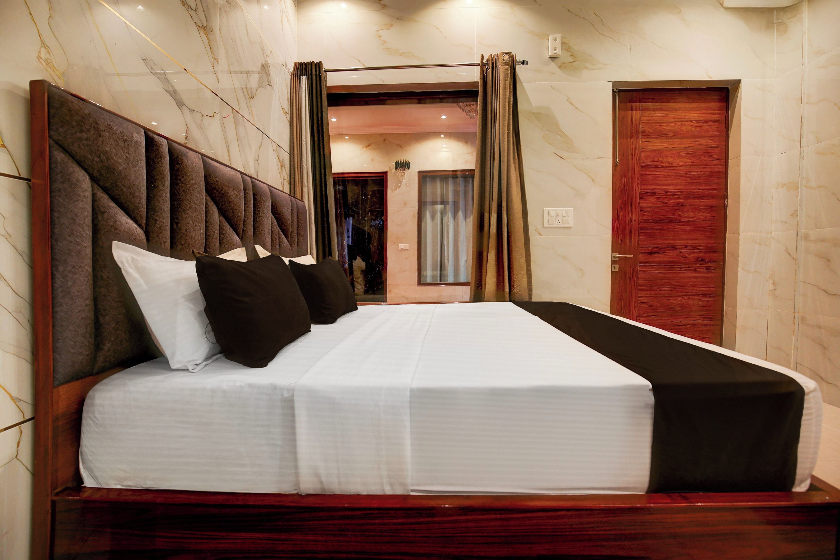 A hotel room with a large bed, a wooden headboard, and marble walls.
