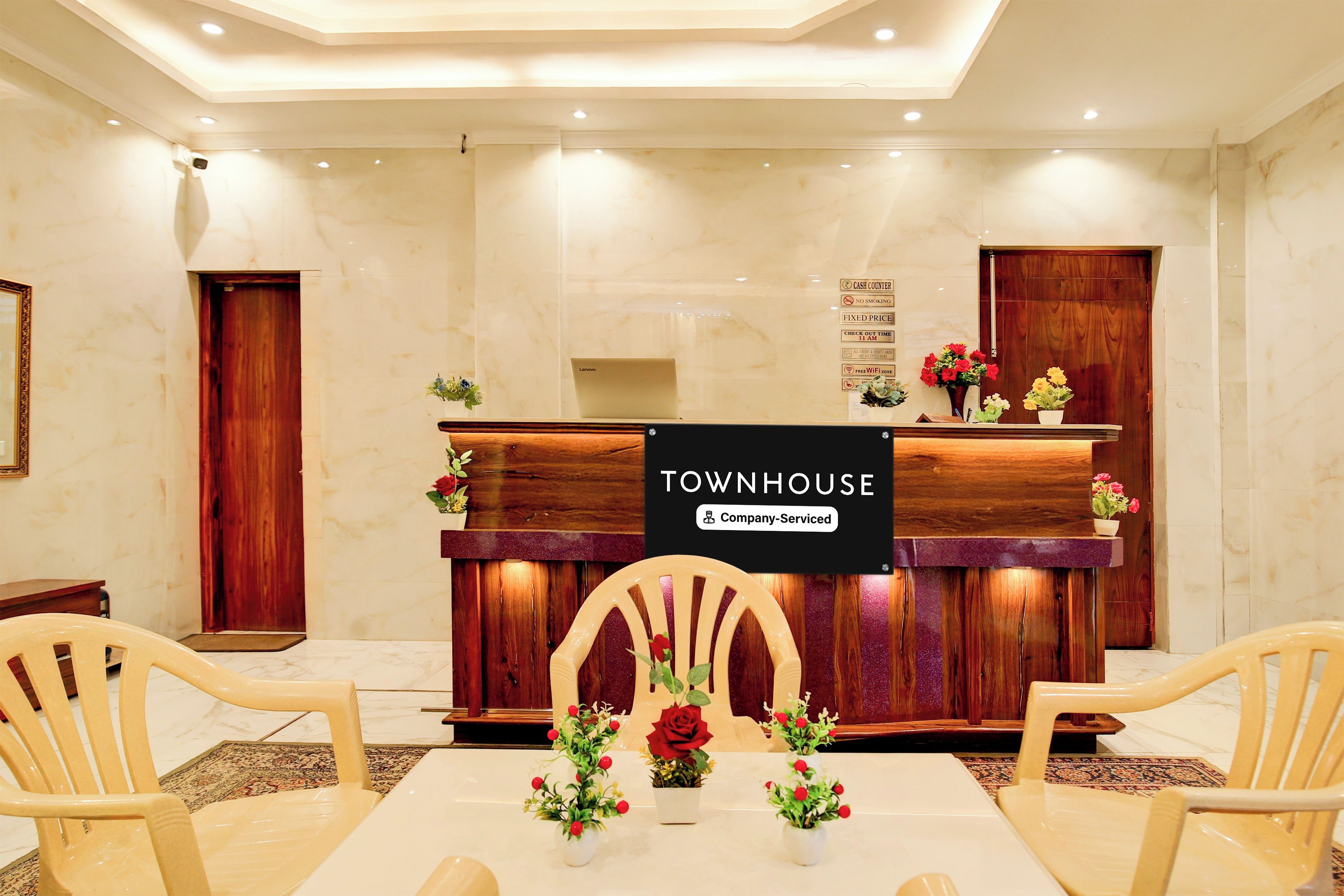 Uma área de recepção com balcão de madeira, duas cadeiras, uma mesa e um aviso indicando 'TOWNHOUSE Company-Serviced'.
