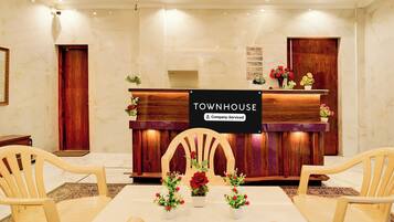 Uma área de recepção com balcão de madeira, duas cadeiras, uma mesa e um aviso indicando 'TOWNHOUSE Company-Serviced'.