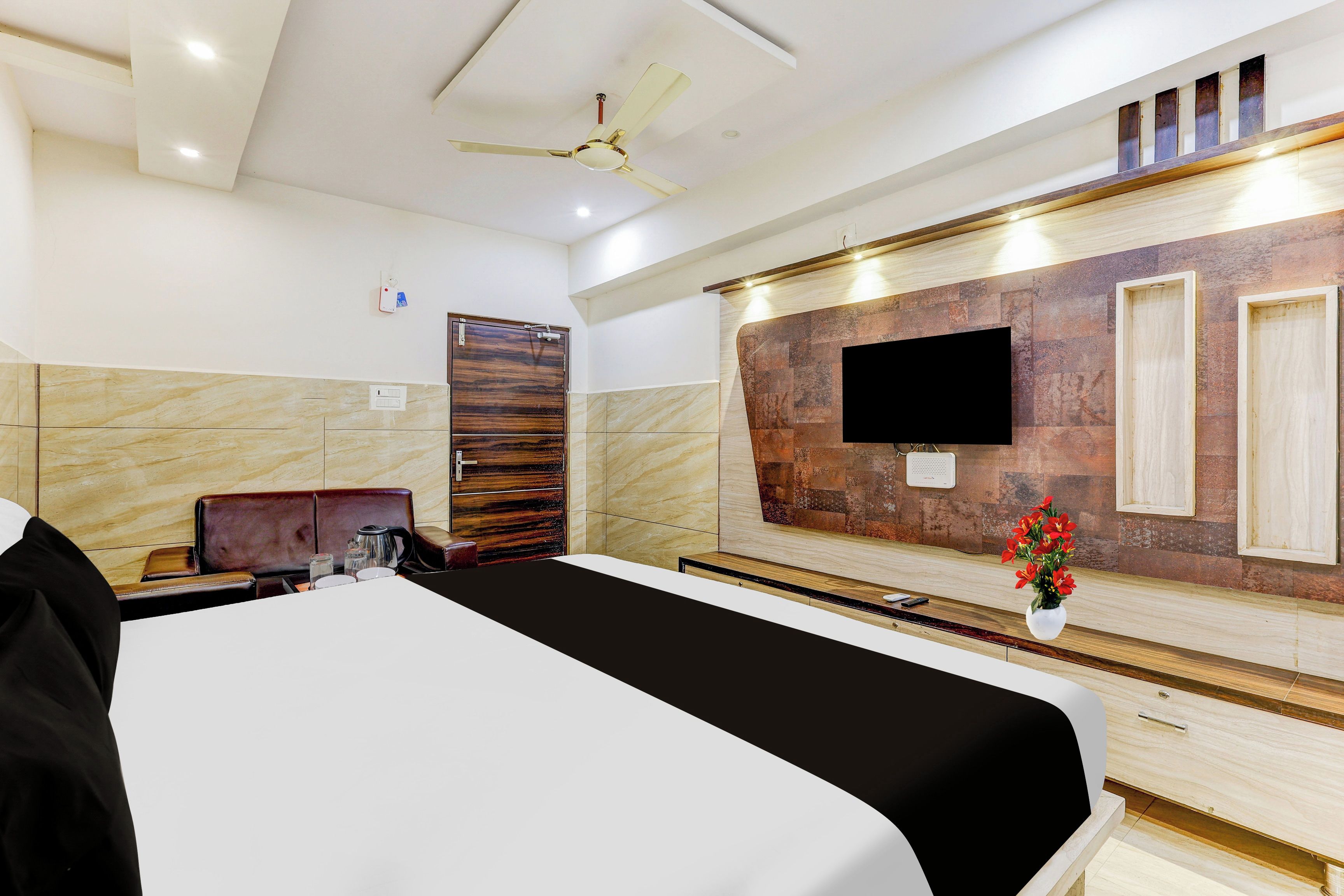 A hotel room with a bed, a desk, a chair, a television mounted on the wall, and a ceiling fan.