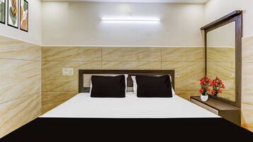 Una habitación de hotel con cama, mesita de noche, espejo y una lámpara de pared.