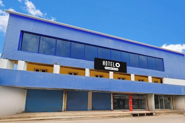 A hotel building with a blue facade, a signboard with the word 'HOTEL' and 'Company-Sponsored' text, and closed shutters on the ground floor.