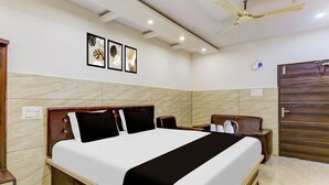 A hotel room with a large bed, a ceiling fan, marble walls, and framed artwork. - Super Hotel O Eluru Railway Station (Eluru)