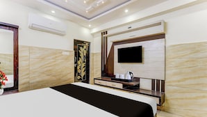 Quarto de hotel com cama, televisão na parede, uma mesinha com chaleira e porta decorativa.