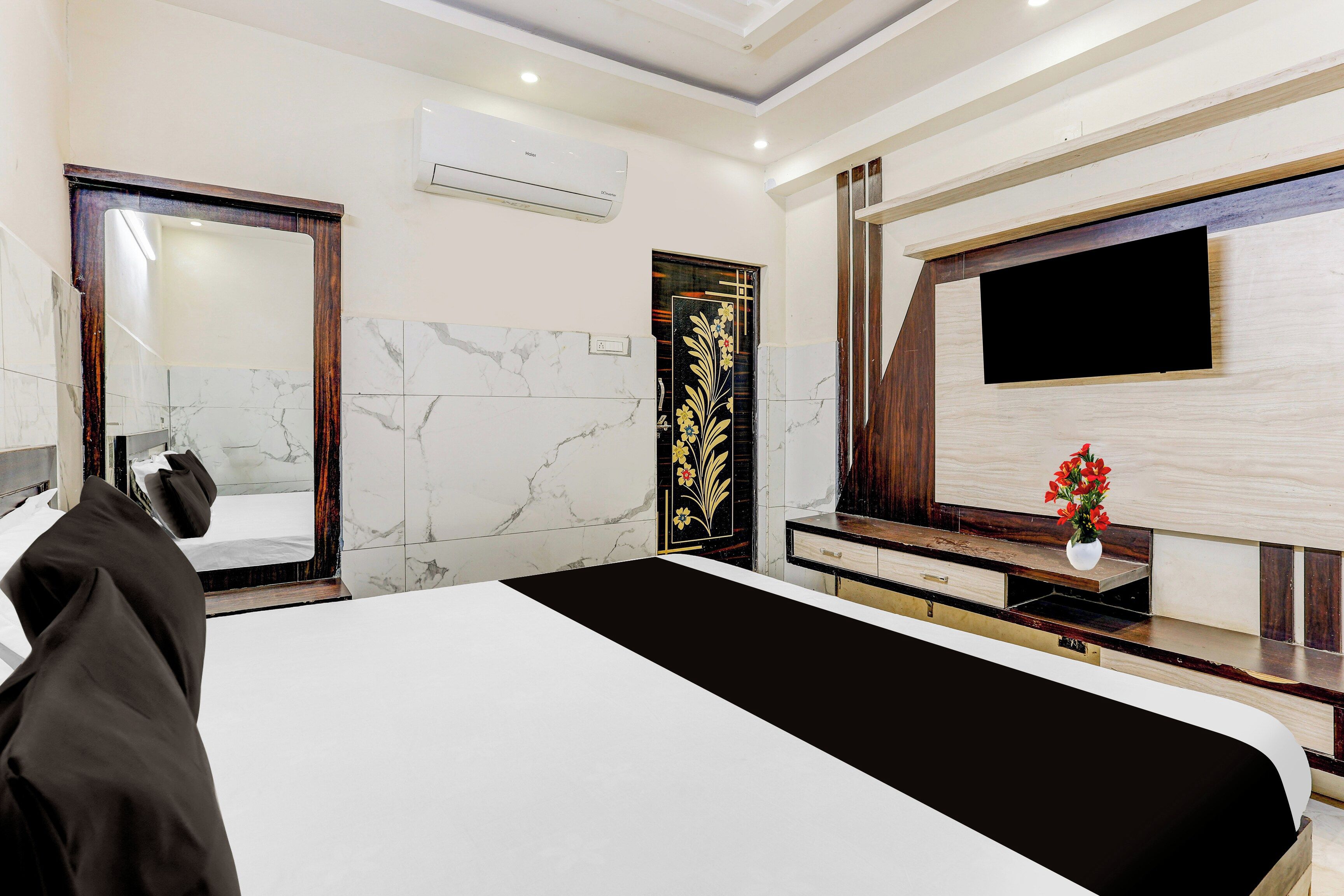 A modern hotel room with a large bed, a flat-screen TV mounted on the wall, and a wooden vanity with a mirror.