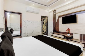 A modern hotel room with a large bed, a flat-screen TV mounted on the wall, and a wooden vanity with a mirror.
