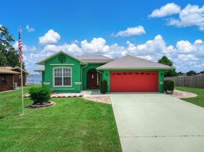 A single-story house with a green exterior, a red garage door, and a well-maintained lawn. - Crane Cabin - Luxurious and spacious 3/2 house on Lake Sebring (Sebring)