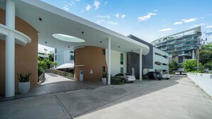 A modern building with a covered entrance, a parking area, and a multi-story structure in the background. - Modern Studio at Twin Sands - Pools & Near Beach (Tambon Patong)