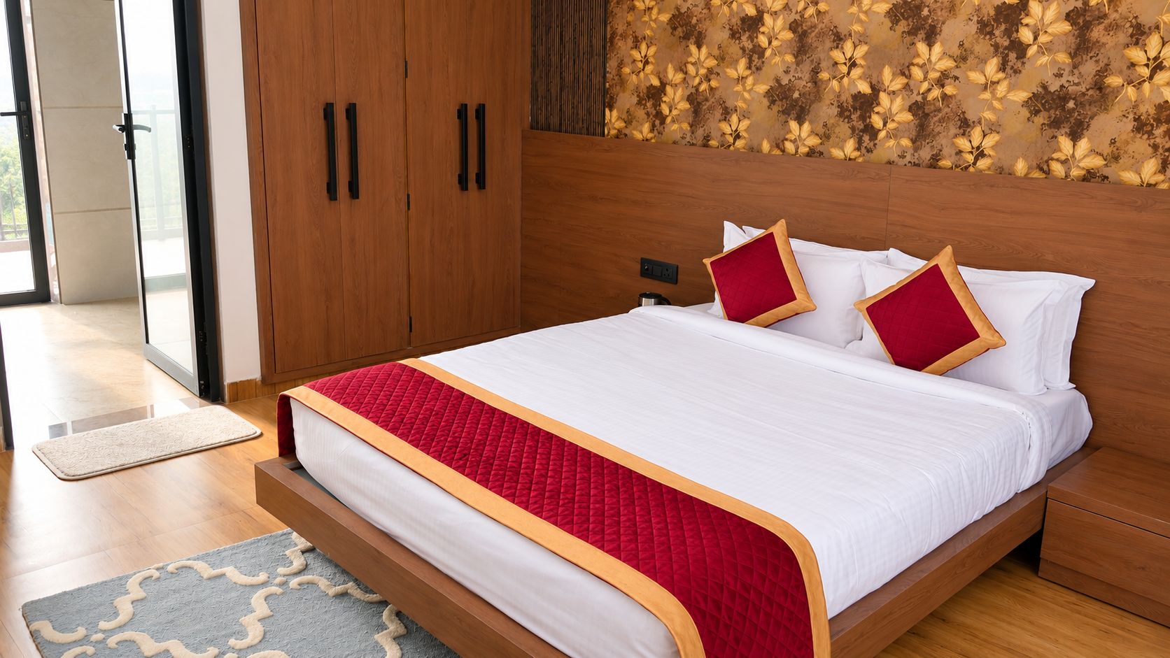Habitación de hotel con cama de madera, ropa de cama blanca, almohadas rojas decorativas, cabecera de madera y pared con estampado.