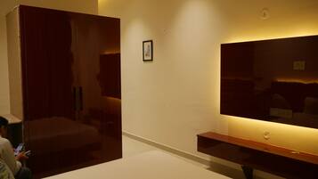 A room with a large wardrobe, a flat-screen TV mounted on the wall, and a small framed picture on the wall.