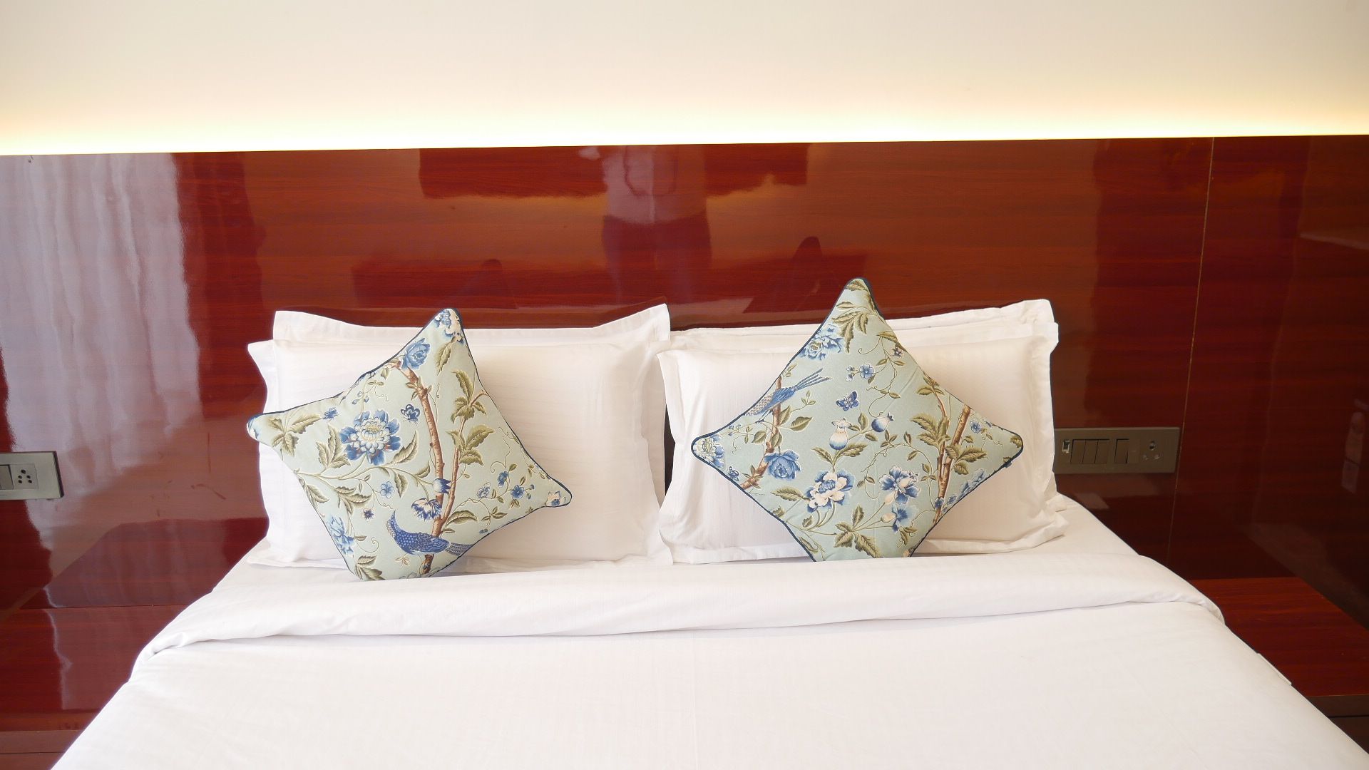 Una cama con ropa de cama blanca y dos almohadas decorativas con motivos florales.