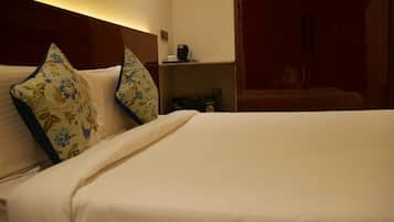 A hotel room with a bed, pillows, a coffee maker, and a shelf with a bottle.