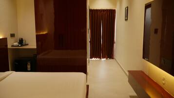 Quarto de hotel com cama, escrivaninha com computador, espelho e janela com cortinas.