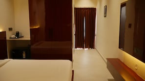 A hotel room with a bed, a desk with a computer, a mirror, and a window with curtains. - Hunaariya Farms (Jaipur)