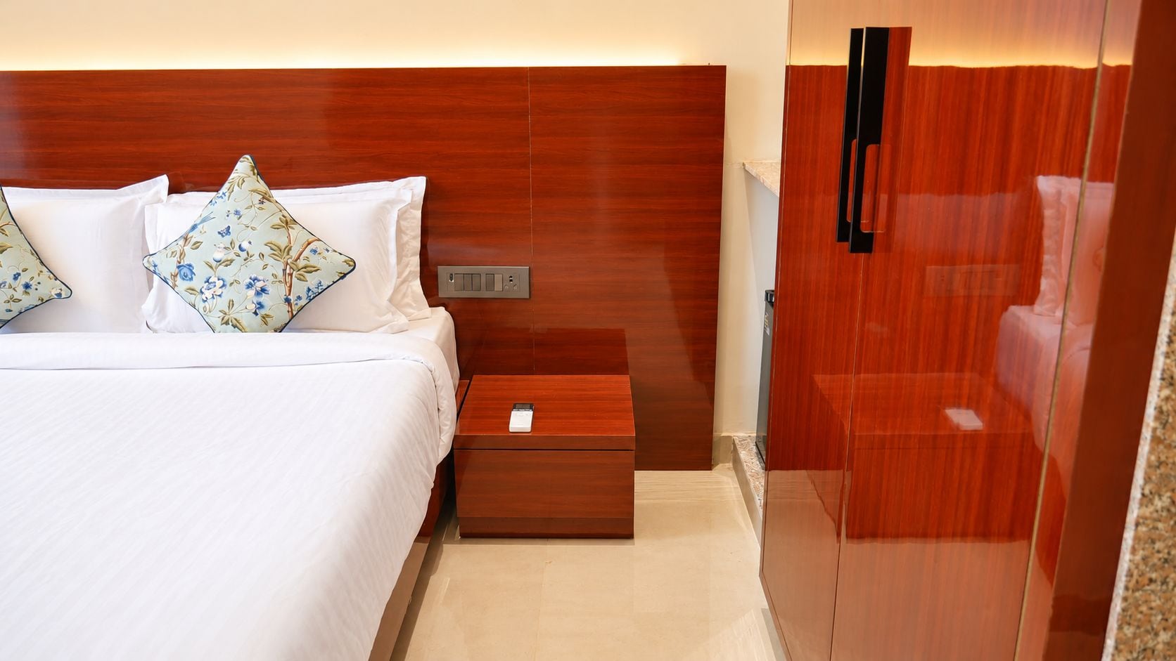 A hotel room with a bed, a nightstand, a wooden wardrobe, and a mirror.