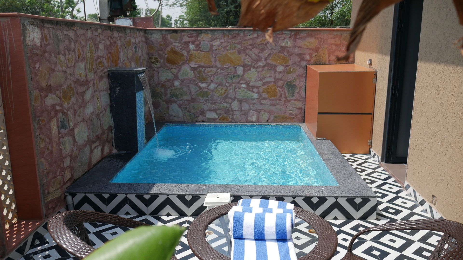 Uma banheira de hidromassagem pequena ao ar livre, com um painel de parede de pedra, piso de azulejo e um armário próximo.