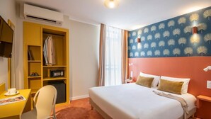 Una habitación de hotel con cama, escritorio con silla, armario y televisor en la pared.