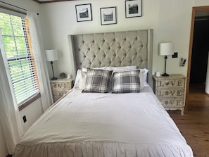 A bedroom with a tufted headboard, a bed with white bedding, two nightstands with lamps, and a dresser with the word 'LOVE' on it.
